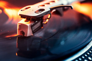 A close up shot of a running record player spinning out some music, dramatically lit with orange light.  Horizontal with copy space.