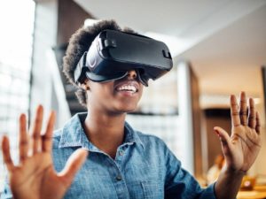 Smiling african woman wearing virtual reality headset in office. Young female at startup using VR goggles.