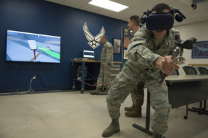 Capt. Patrick Britton, 359th Training Squadron Detachment 1 commander, right, uses a spray gun and HTC Virtual Reality goggles to apply paint to a virtual aircraft part in a 3D VR trainer Dec. 12, 2018, at the unit's schoolhouse on Naval Air Station Pensacola, Florida. The 359th TRS Detachment 1 recently installed two 3-D virtual reality paint trainers to create a safer and more efficient way of training Airmen. The detachment graduates about 1,200 Airmen annually in the aircraft structural maintenance, low observable aircraft structural maintenance, and non-destructive inspection career fields. (U.S. Air Force photo by Randy Martin)